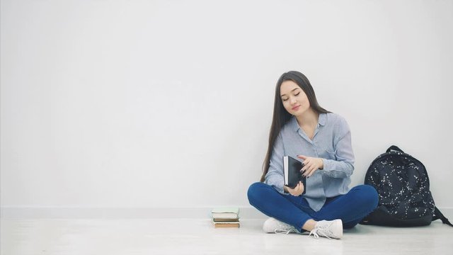 Young asian girl involved in the process of reading book, closing itand hugging, while sitting on the floor in lotos position.