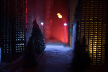 Little miniature city with road and lights. Decorative cute small houses in snow at night in...