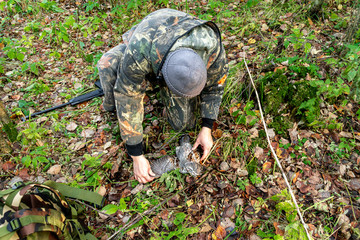 A hunter examines a downed grouse lying on the ground covered with fallen foliage