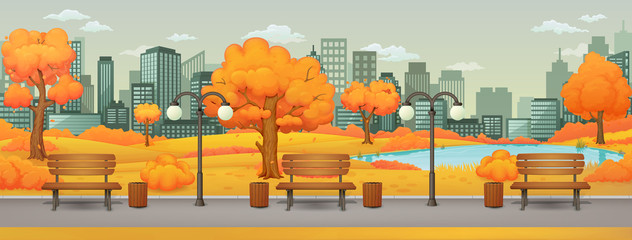 Autumn day park,street scene. Benches with trash cans and street lamps on a trail with orange and yellow trees and bushes. Meadow, lake, skyscrapers and gray sky with clouds in the background.