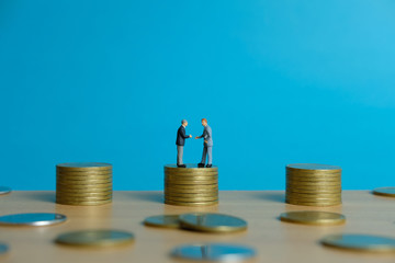 Miniature business concept - two businessman make an handshake for partnership agreement handshake with coin stack