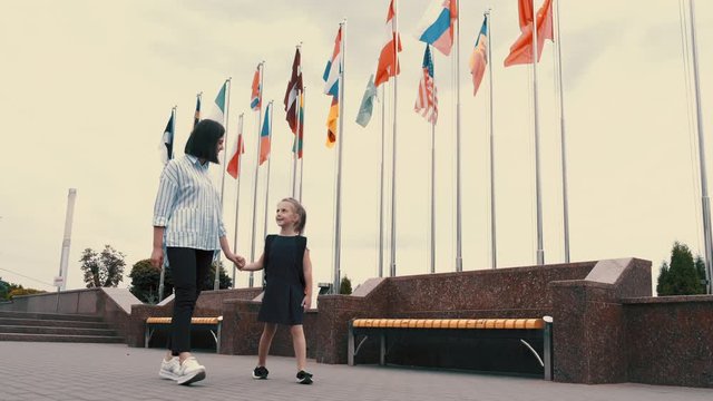The mother and a little daughter are having a walk together. The girl is having free time with mother after her classes. The flags of countries are on the background.