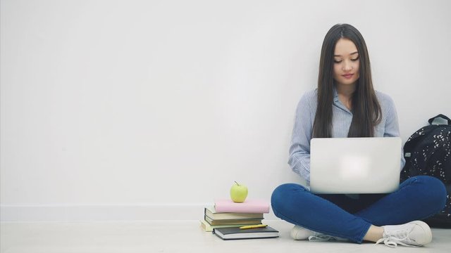 Lovely young asian lady sitting on the floor in lotos position, with laptop, pointing her fingers at the camera, then to the side, smiling.