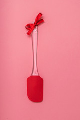 Red kitchen spatula with red ribbon on pink background. Flat lay.