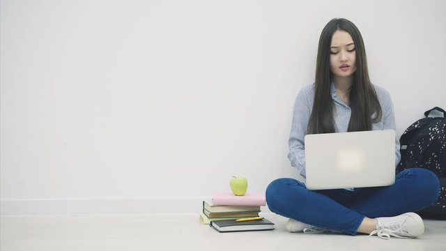 Tired young asian lady sitting on the floor in lotos position, with laptop, yawning, making a break, eating apple.