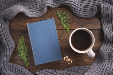 Winter, cozy composition. Warm scarf, book and cup of coffee, on wooden background. Flat lay, top view, copy space.