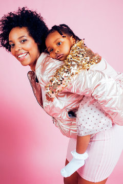 young pretty african-american mother with little cute daughter hugging, happy smiling on pink background, lifestyle modern people concept