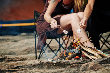 Cropped image of travelers using sticks when frying marshmallows on fire - Powered by Adobe