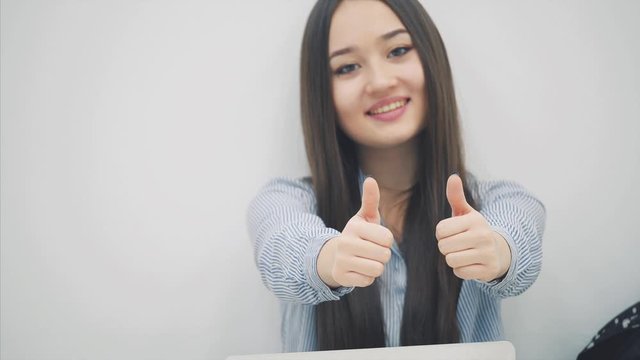 Lovely asian girl with long hair sitting with laptop on her knees, looking at the camera, giving thumbs up.