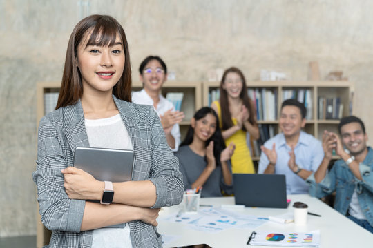 Leadership Asian Creative Woman Or Head Staff Employee Feeling Happy And Smiling Is Standing Out Of Small Group Clapping Hands In Creative Office Workplace. Woman Feeling Confident With Smiling Face.