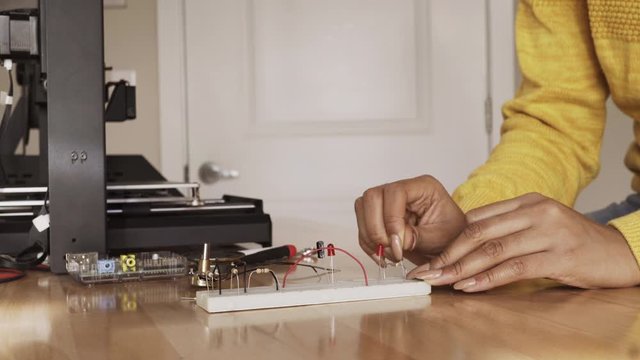 Young Black Woman Engineering Student Working on Breadboard Near 3D Printer