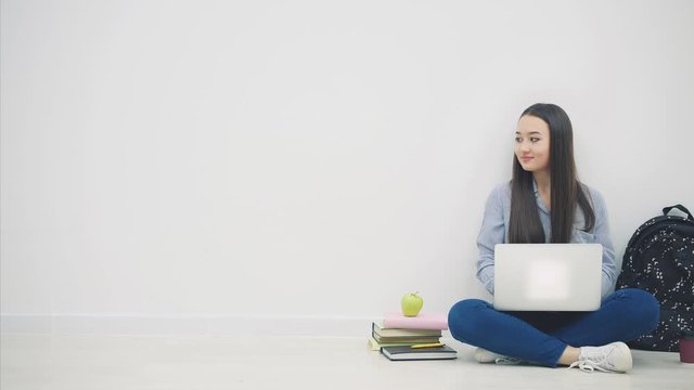 Lovely young asian lady sitting on the floor in lotos position, searching in the internet, nodding her head. School supplies around her.
