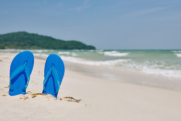 Bright blue flip-flops in sand on the beach, sea waves in background