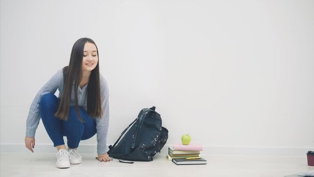 Adorable young asian girl appearing on white background, sitting down on the floor in lotos position, closing up her backpack, standing up, disappearing .