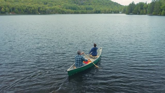 Aerial: Father and daughter paddling in a canoe on a calm blue lake. Quebec, Canada. 