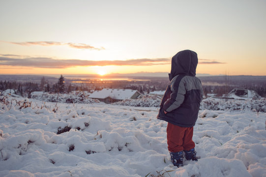 little boy watching the sunset in winter snow