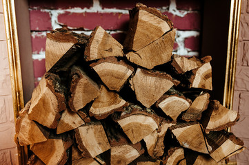 felled tree, a lot of firewood stacked on top of each other indoors against the background of a red brick wall