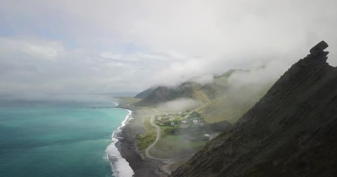 Drone shot of cliff near great beach with blue water and white waves. Sliding down the cliff. Beautiful clouds flowing over the mountains.