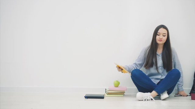 Adorable young asian girl sitting on the floor in lotos position, with sketchbook in her hands, looking up, nodding her head, smiling.