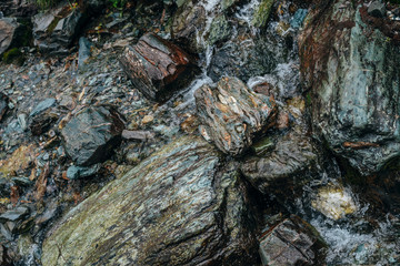 Clear spring water flows on beautiful stony pile slope. Boulder stream with small mountain creek. Wet shiny stones close-up. Nature background with small highland brook. Clear water stream on boulders