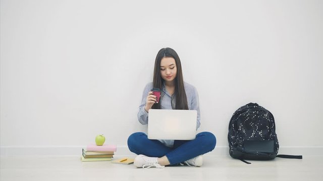 Smiling asian female student sitting in lotos position, using laptop, drinking coffee.