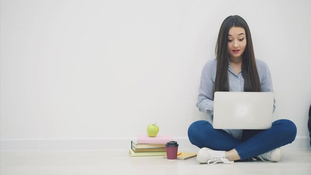 Asian female student sitting in lotos position, using laptop, drinking coffee. She has pain in her fingertips because of typing.