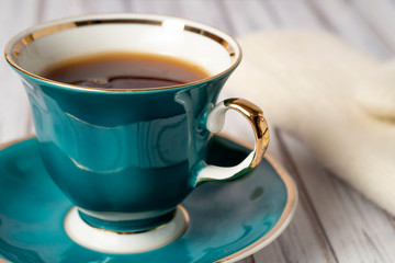 Green cup of hot tea and white mittens on a wooden table. Close up