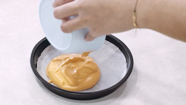Young female scoops out cake mixture into cake pan