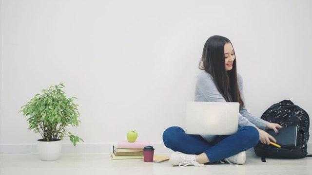 Asian lady sitting on the floor in lotos position, found something interesting in her laptop and decided to copy it into her notebook.