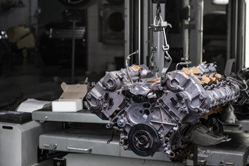 Used v8 engine with eight cylinders suspended mounted on a crane for overhaul repair and installation on a car after a breakdown in the vehicle workshop. Auto service industry. Сylinder scratches.