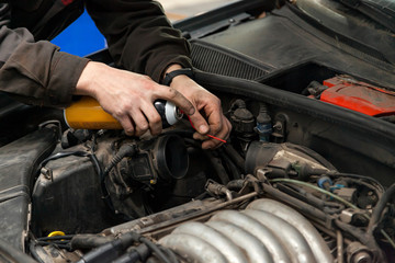 A male mechanic with a can spray gasoline into the intake manifold to start the car during engine breakdown of the ignition and fuel supply system in a vehicle repair workshop. Auto service industry.