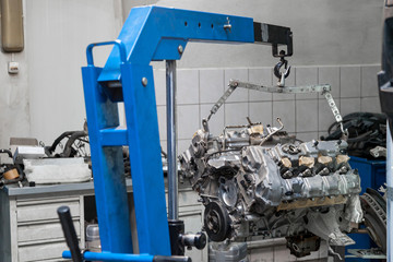 Used v8 engine with eight cylinders suspended mounted on a crane for overhaul repair and installation on a car after a breakdown in the vehicle workshop. Auto service industry. Сylinder scratches.