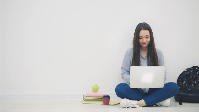Asian lady sitting on the floor in lotos position, with laptop, raising up her hands, smiling happily as a winner.