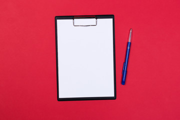 Clipboard with white sheet and pen on a red background. View from above. space for text