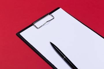 Clipboard with white sheet and pen on a red background. View from above. space for text