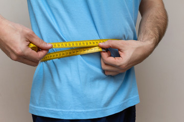 man in a blue T-shirt measures the waist with a yellow tape
