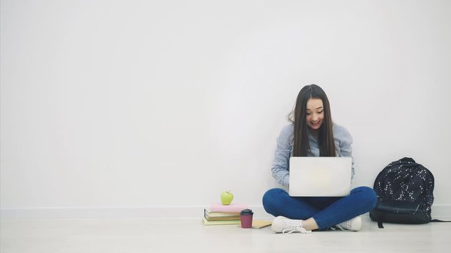 Asian lady sitting on the floor in lotos position, with laptop, raising up her hands, waving them and smiling happily as a winner.