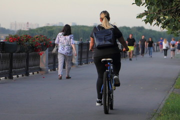 Obraz premium A woman with long hair on a Bicycle ride on an asphalt road in the Park on a summer Sunny evening, active urban recreation