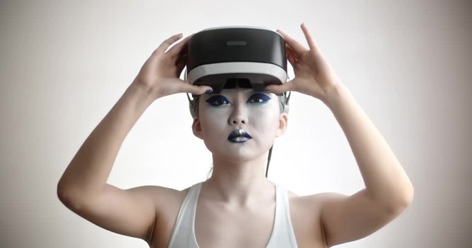 Young asian girl with bright artistic make-up wearing a vr helmet diving in world of vitual reality, moving her hands and interacting with it - technology concept closeup 4k footage