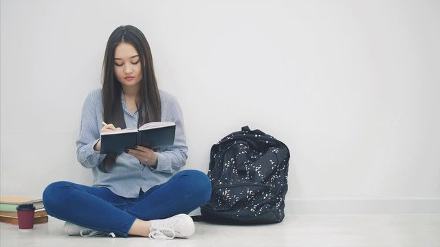 Inspired young asian girl sitting on the floor, finished writing, took out phone and headphones out of her backpack, and is going to listen to music.
