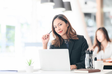  businesswoman holding pencil, smailing and looking at camera while sitting in modern office.