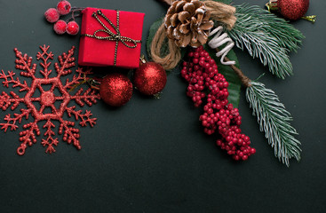 Black festive Christmas background with contrasting red spruce branches, cones, spruce toys, snowflakes and a surprise in a gift box and red berries