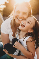 Portrait of a lovely mother and daughter laughing while mother is embracing her girl against sunset...