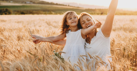 Portrait of a happy young mother and her lovely daughter playing and laughing in a field of wheat ....
