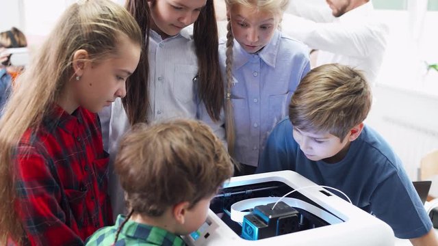 Education in the modern school, children learn modeling, boys and girls watching of process 3D printer prints.