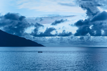 Stunning purple tropical sunset. In the distance there is a dark silhouette of a boat with people