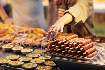 Female customer taking skewer with fried meet from stall with Asian street food