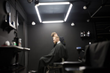Blurred photo of a barber shop room in black style and lamps.
