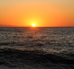 the sun setting behind the promontory with the sea in the foreground