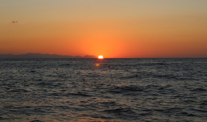 the sun setting behind the promontory with the sea in the foreground